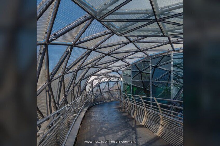 A glass-structured pedestrian bridge with a metal framework and a walkway. 3