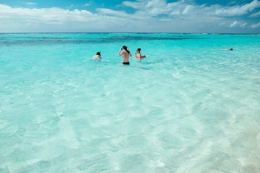 A clear turquoise sea with people swimming and walking in shallow water. 4
