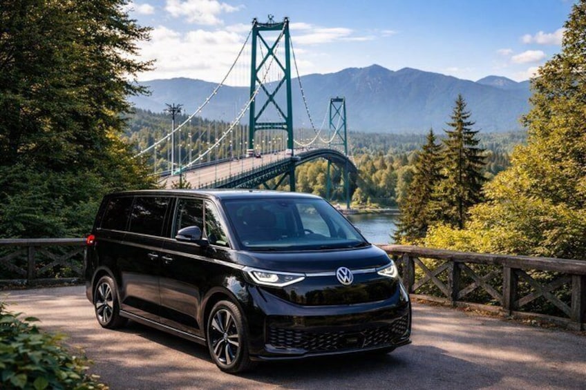 Un SUV nero parcheggiato su una strada con un ponte verde e montagne sullo sfondo. 1