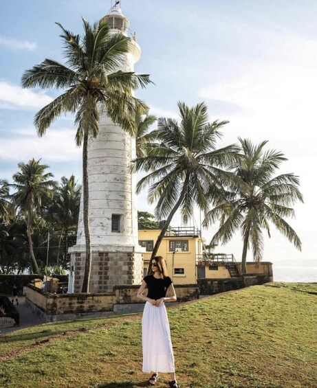 A person standing in front of a lighthouse with palm trees in the background. 5