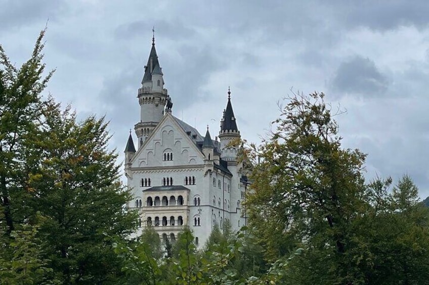 A large, white castle with multiple towers and a prominent spire, surrounded by lush greenery. 2