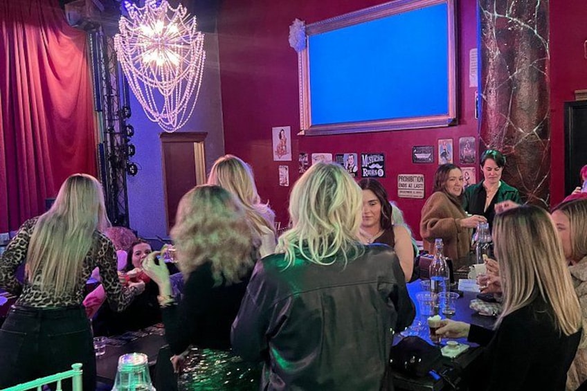 Un grupo de personas en un evento social, con una araña de cristal, una pantalla y varios carteles en la pared. 3