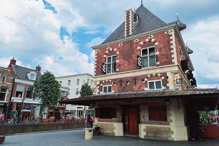 A red brick building with a gabled roof, a covered entrance, and a street with bicycles and pedestrians. 4