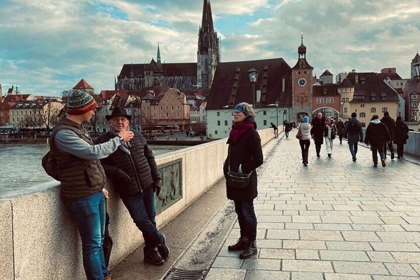 A bridge with people walking, a river, and historic buildings in the background. 4