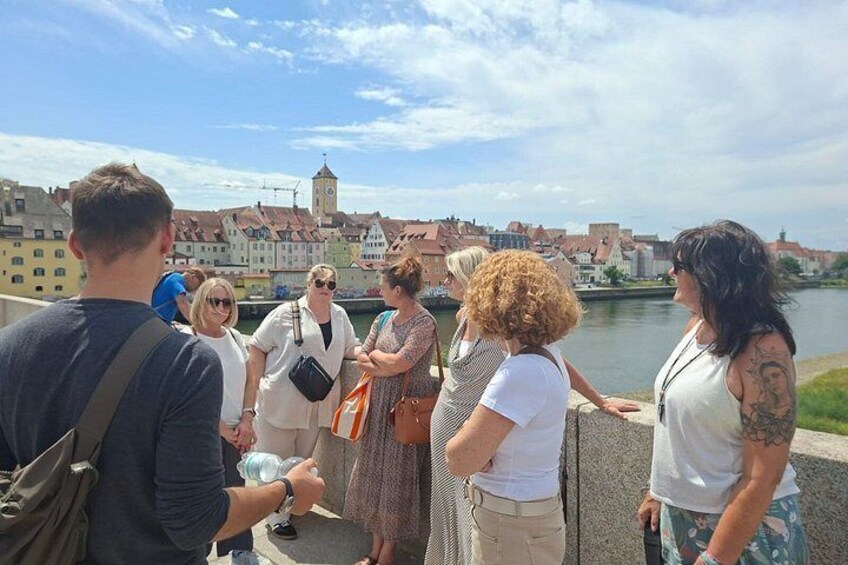 A group of people standing on a bridge overlooking a river with buildings and a clock tower in the background. 5