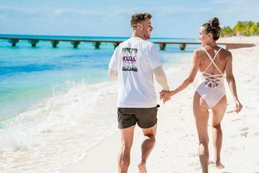Een paar mensen wandelen over een strand, met een pier op de achtergrond. 1