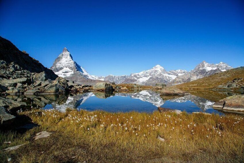 Un lago de montaña con el reflejo de un pico nevado, rodeado de terreno rocoso y vegetación escasa. 4