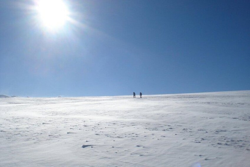 Paisaje nevado con dos personas caminando a lo lejos bajo un cielo despejado. 3