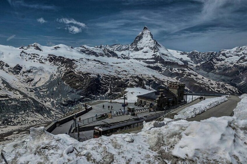Una montaña nevada con un pico destacado, un centro de esquí con edificios y un teleférico, y una carretera que conduce al centro. 2