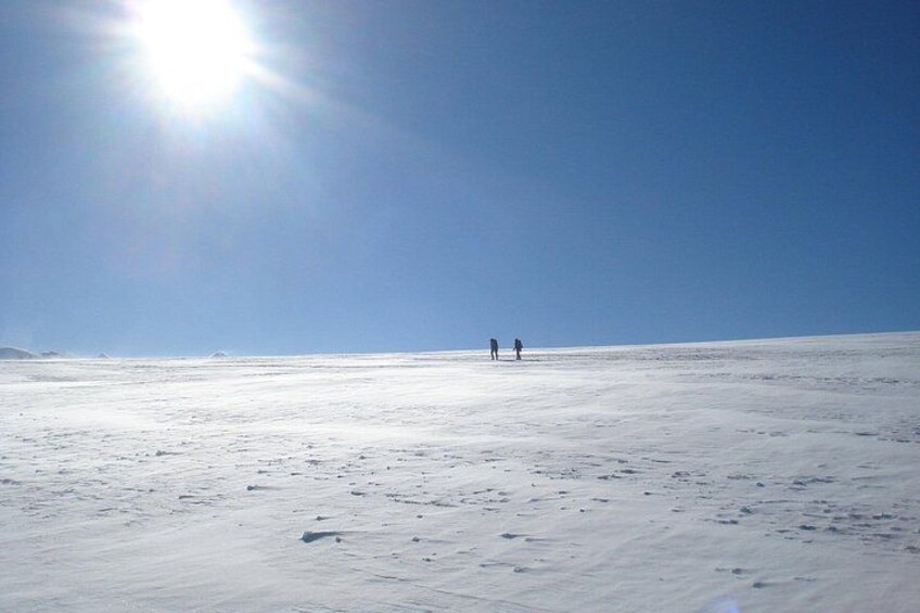 Ett snöigt landskap med två personer som går på avstånd under en klar himmel. 3