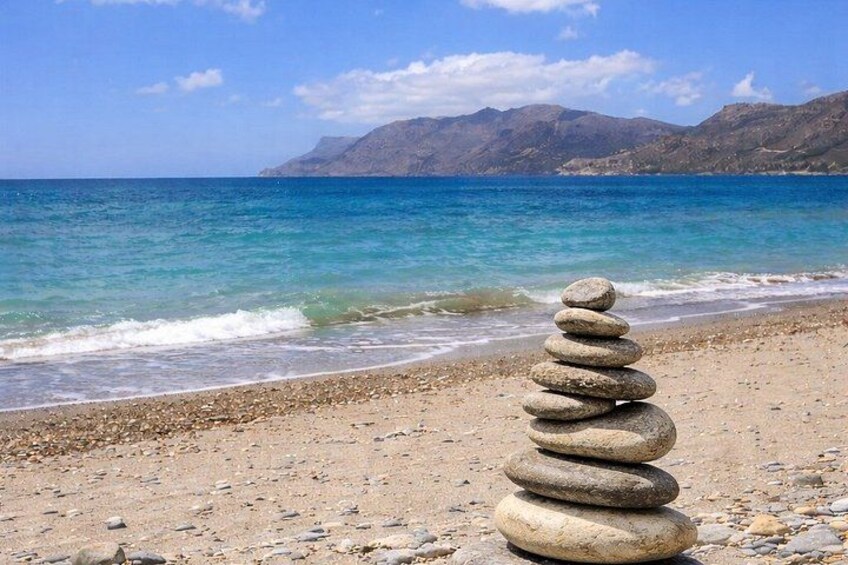 A stack of stones on a beach with a mountain and ocean in the background. 1