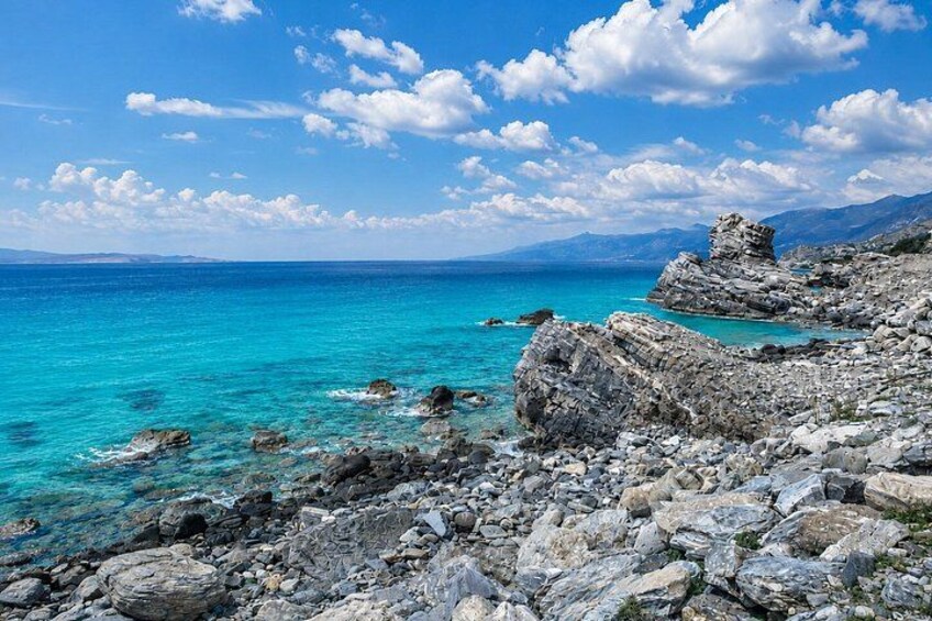 A rocky coastline with clear turquoise waters and distant mountains under a partly cloudy sky. 3