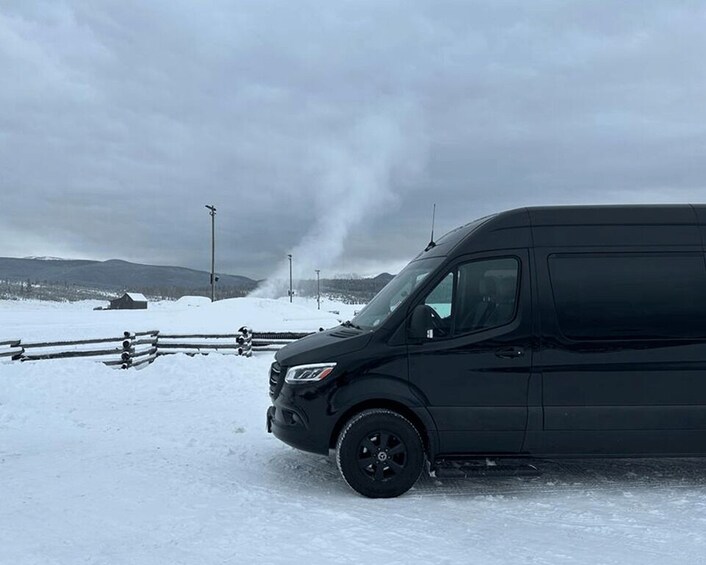 A black SUV parked on a snow-covered road with a wooden fence and a mountain in the background. 2