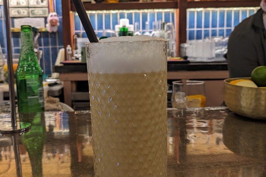 A glass of beer with a straw, a green bottle, and a bar counter with various items in the background. 4