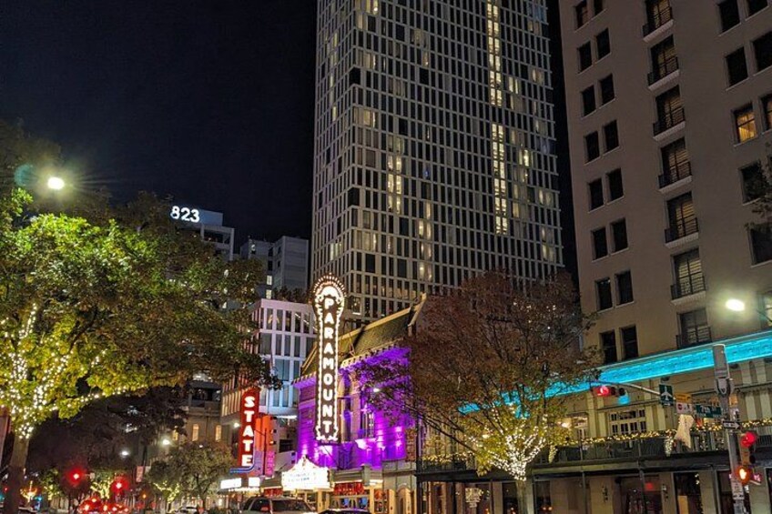 A brightly lit theater marquee, a street with trees, and tall buildings in the background. 5
