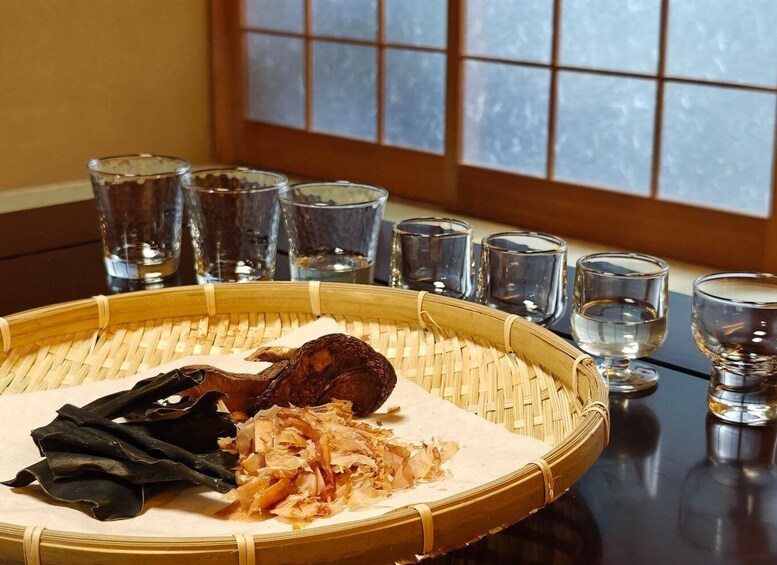 A traditional Japanese meal setup with a woven tray, dried seaweed, and shredded vegetables, accompanied by six clear glasses. 3