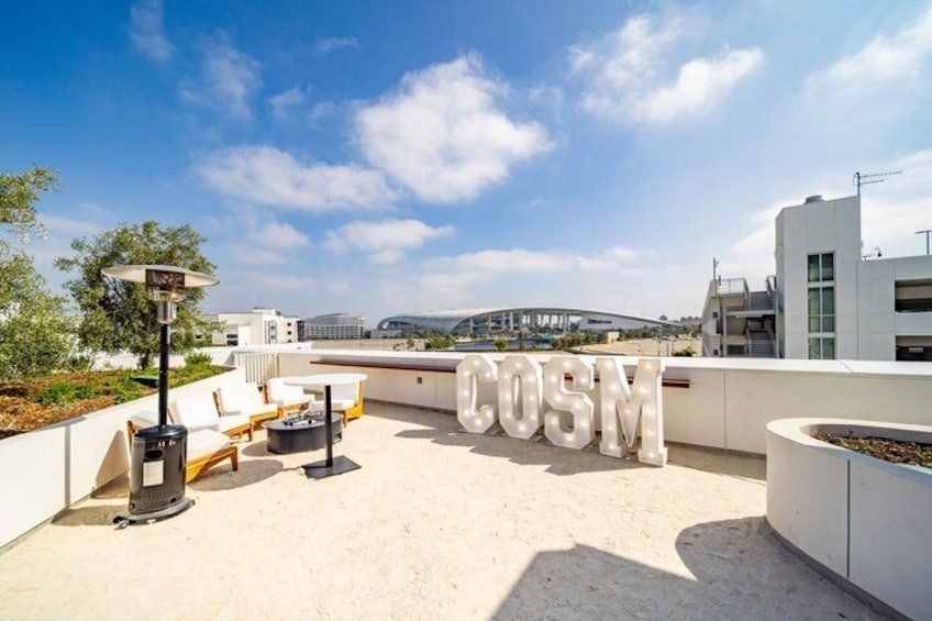 A rooftop terrace with lounge chairs, a large 'COSM' sign, and a cityscape in the background. 3