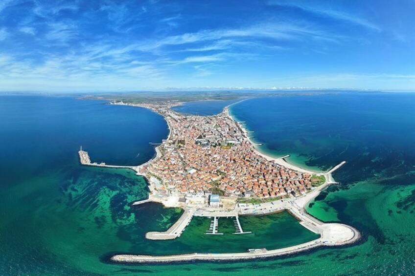 An aerial view of a coastal town with a curved harbor, a lighthouse, and a prominent white building. 1
