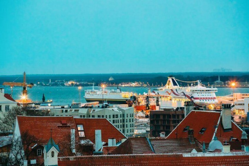 Un paisaje urbano costero al atardecer con un crucero amarrado, edificios con tejados rojos y un puente al fondo. 4