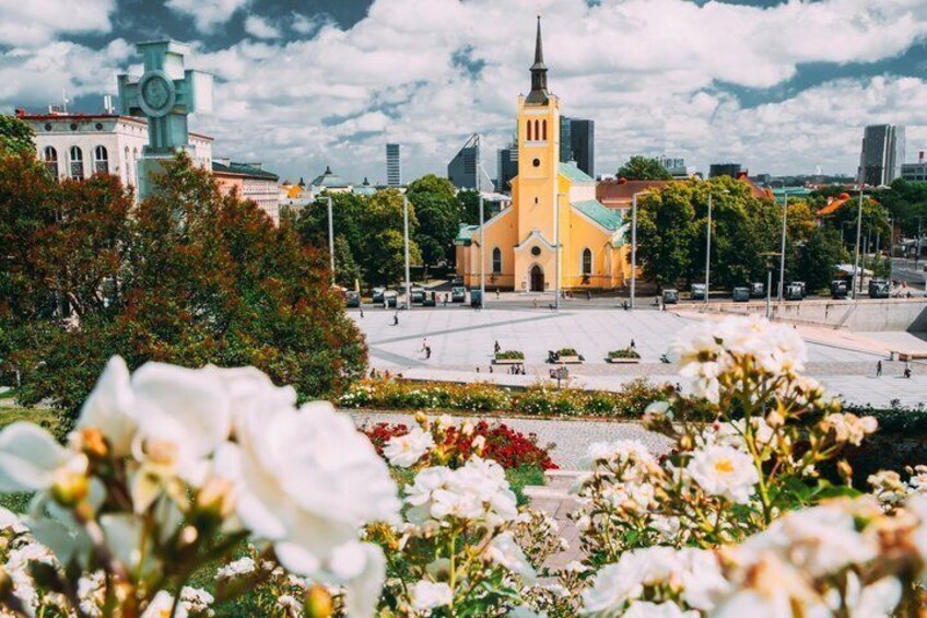 Una iglesia con una aguja alta, una torre de reloj y una plaza llena de flores. 5