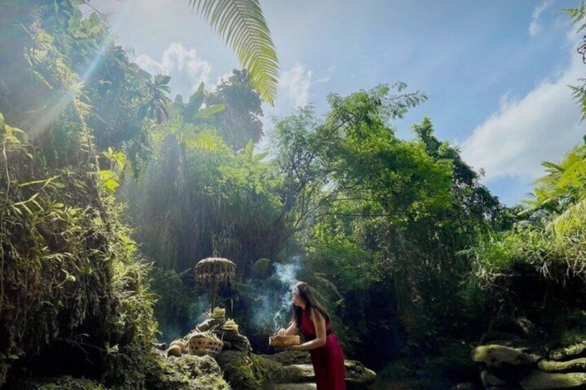 Una persona con vestido rojo de pie cerca de una formación rocosa con humo o neblina ascendiendo, rodeada de vegetación exuberante y un cielo despejado. 3