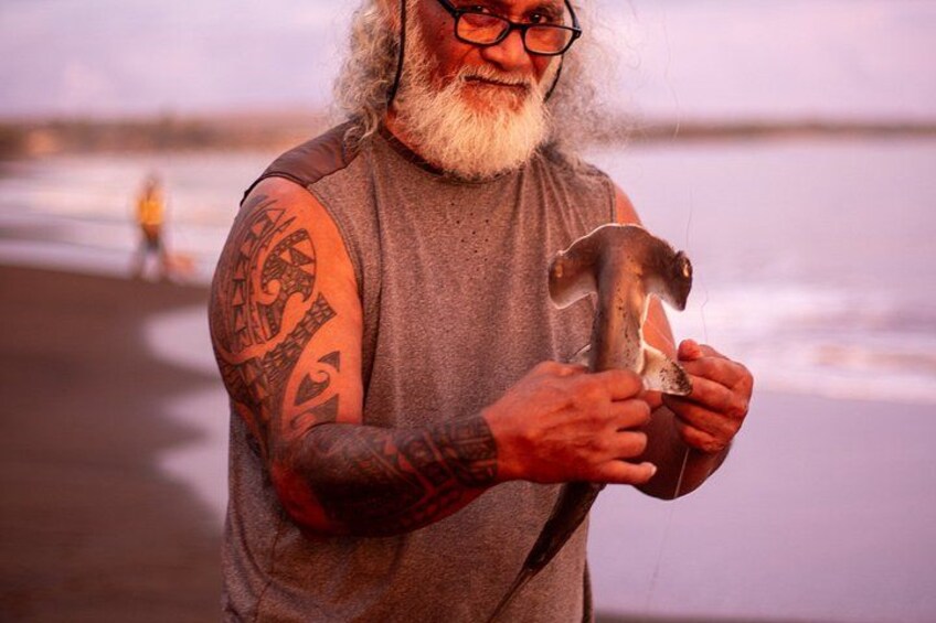 Una persona sulla spiaggia che tiene un martello, con un braccio tatuato. 2