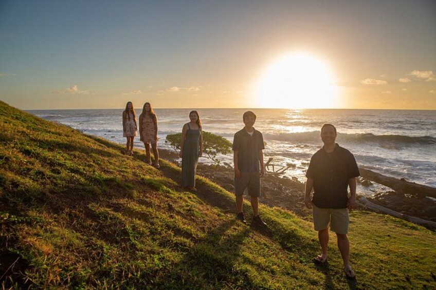 Un gruppo di persone in piedi su una collina erbosa con vista sull'oceano al tramonto. 5