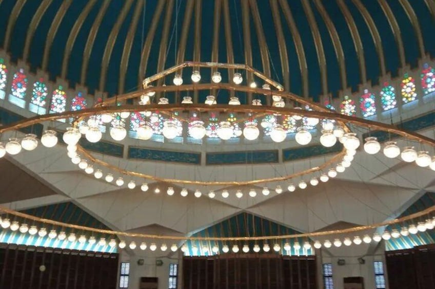 Un candelabro grande y ornamentado con múltiples niveles de luces en un edificio con techo abovedado y vidrieras. 4