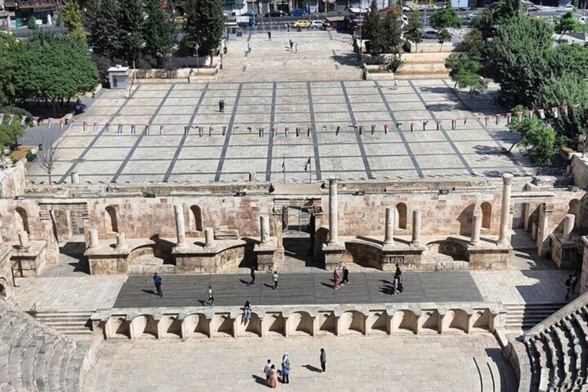 Una amplia plaza abierta con antiguas estructuras de piedra, incluyendo columnas y arcos, rodeada de árboles. 2