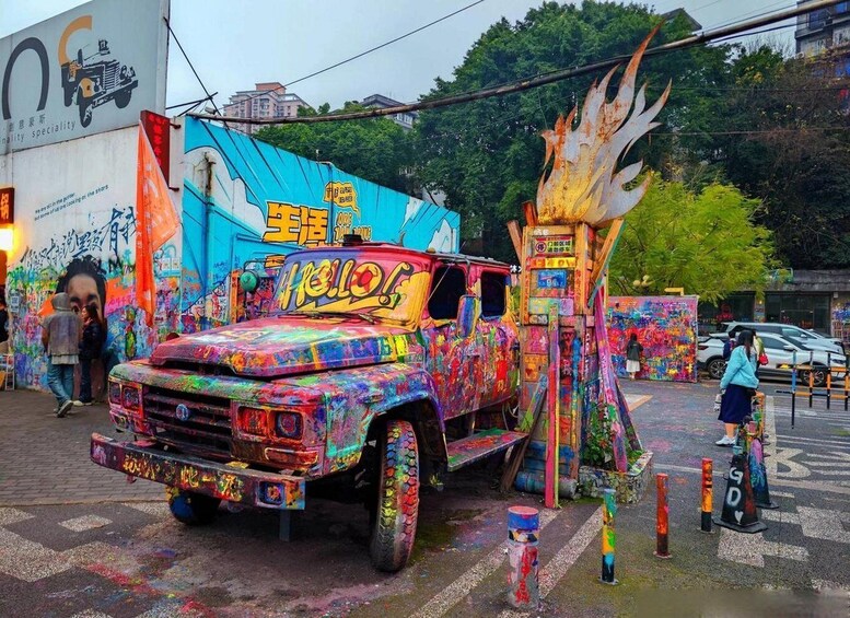 A colorful, graffiti-covered truck parked on a street with a mural in the background. 3