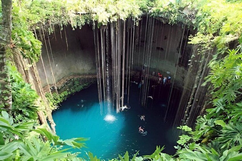A natural pool with clear blue water surrounded by lush greenery and a rocky cave entrance. 5