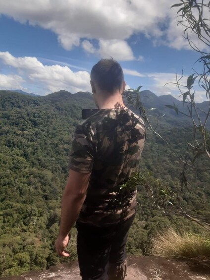 A person standing on a cliff overlooking a dense forest and mountains. 2