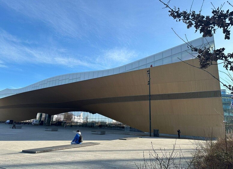 A modern architectural structure with a unique curved roof, a clear sky, and a few people in the foreground. 2