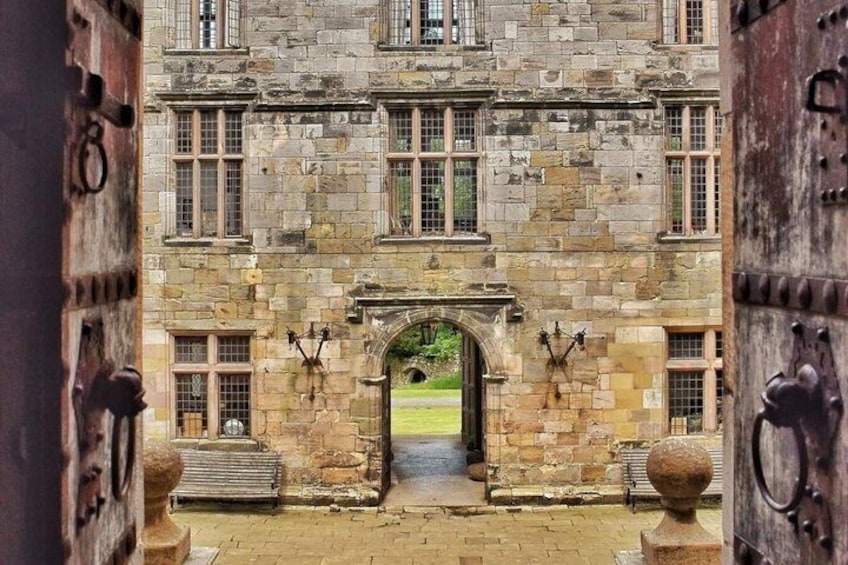 A stone building with a central archway, large wooden doors, and a paved courtyard. 3