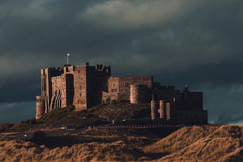 Un castillo histórico en una colina con una bandera, rodeado de un paisaje cubierto de hierba. 1