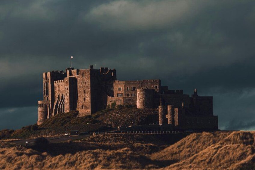 A medieval castle on a hill with a flag, surrounded by a grassy landscape. 1
