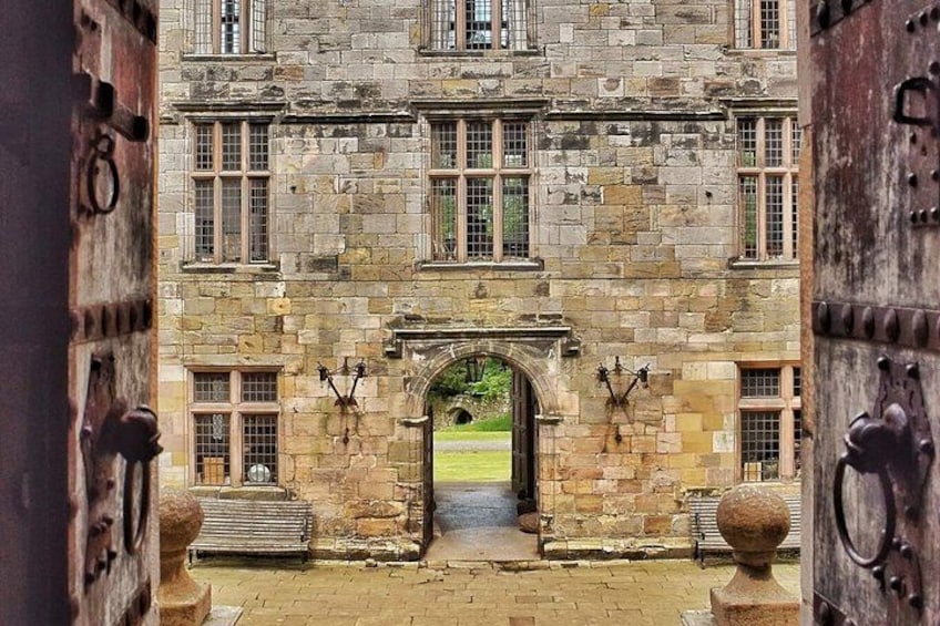 A stone building with a large arched entrance, a brick pathway, and a grassy area beyond. 2