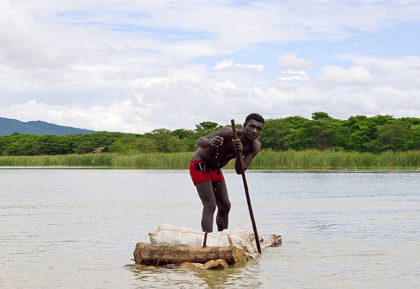 A person standing on a log in a body of water, holding a long pole. 3