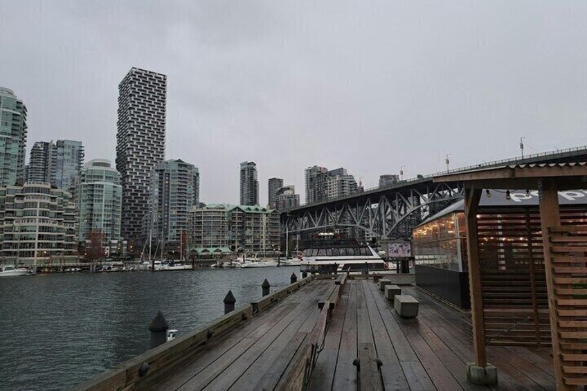 A wooden pier extending into a body of water with a city skyline in the background, including a distinctive tall building with a unique facade. 2