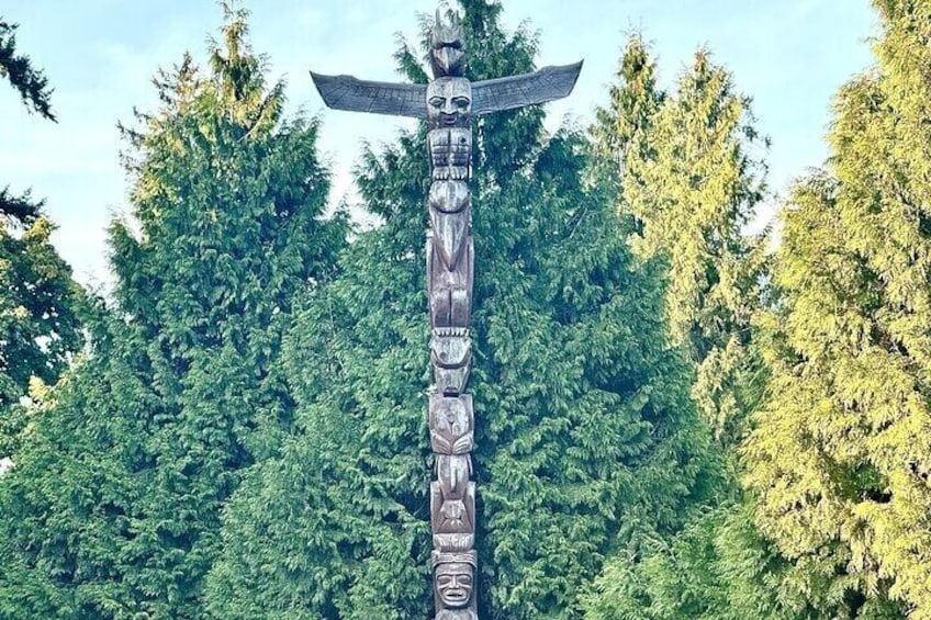 A totem pole with intricate carvings, set against a backdrop of dense green forest. 3