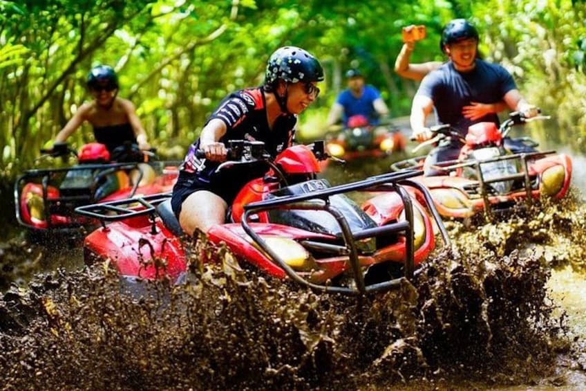 People riding ATVs through a muddy forest trail. 1