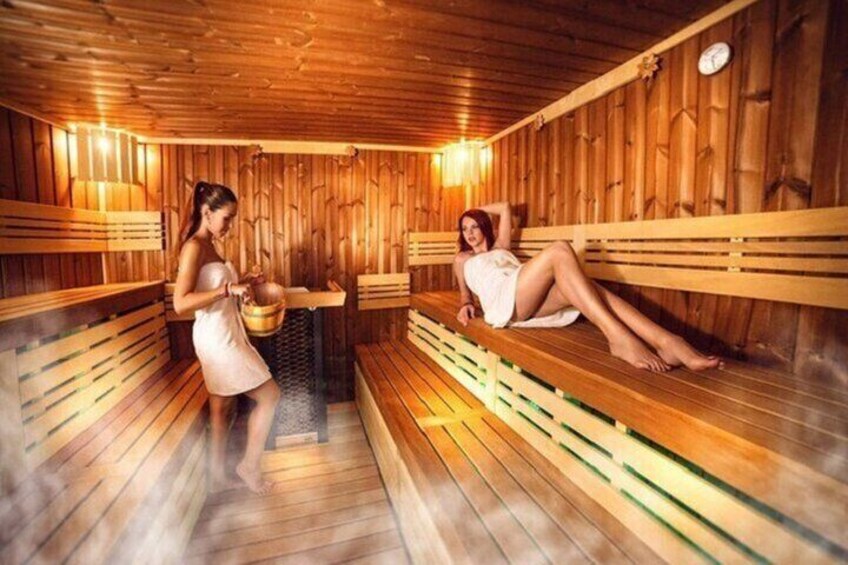 A wooden sauna with benches and a person standing by a bucket. 3