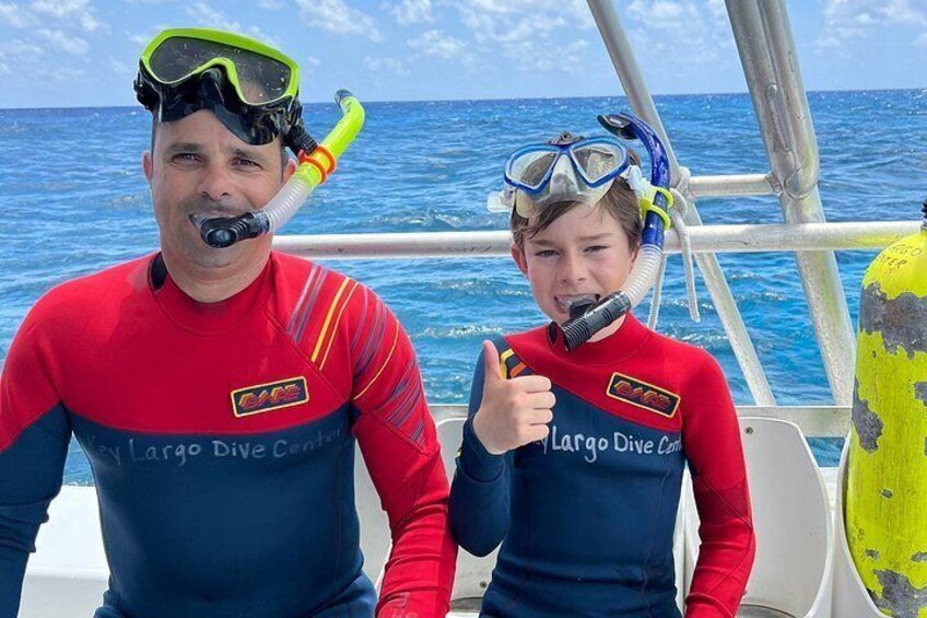 Two people in red and blue long-sleeve shirts with 'Largo Dive Center' on them, sitting on a boat with the ocean in the background. 3