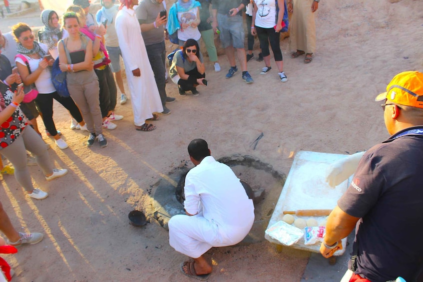 A group of people gathered around a man cooking in a traditional pit. 4