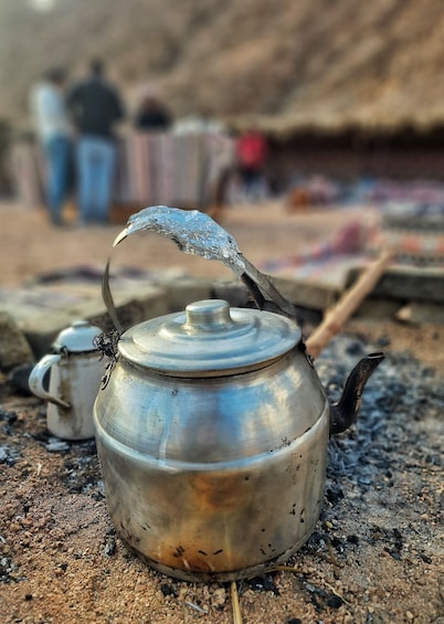 A metal teapot on a stove with a thatched roof in the background. 5