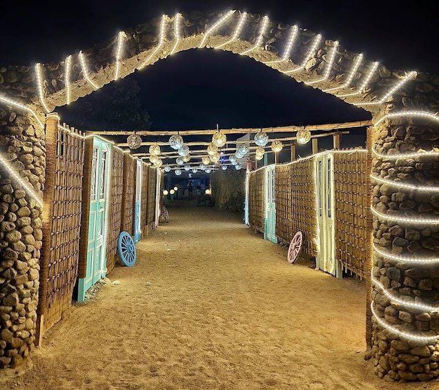 A nighttime pathway flanked by stone walls and wooden doors, illuminated by string lights and hanging globes. 1