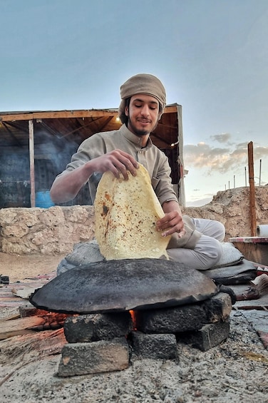 A person cooking flatbread over an open fire. 2