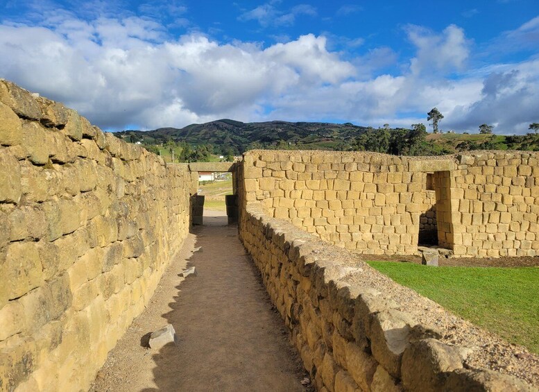 A stone pathway leading through a historical site with stone walls and a grassy area. 3