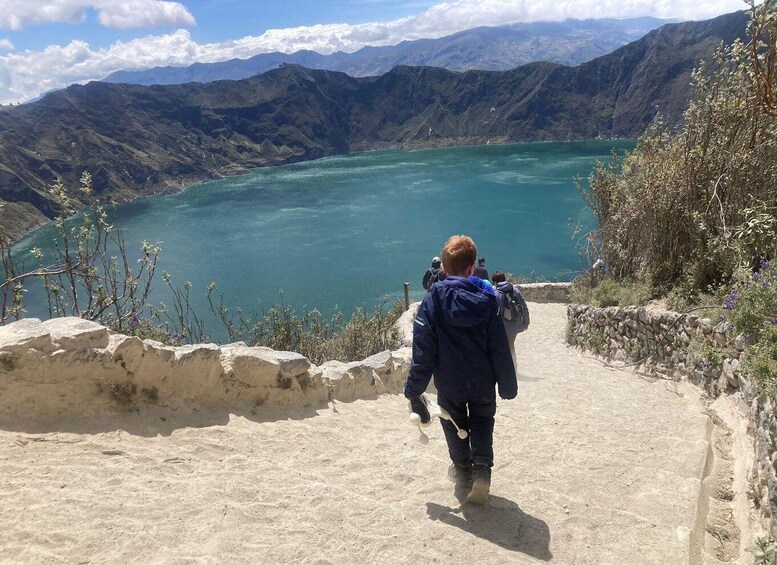 A person walking up a dirt path towards a lake surrounded by mountains. 2