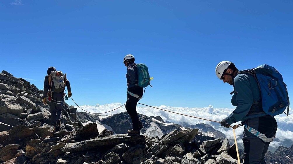Three hikers on a rocky mountain peak with clear skies. 5